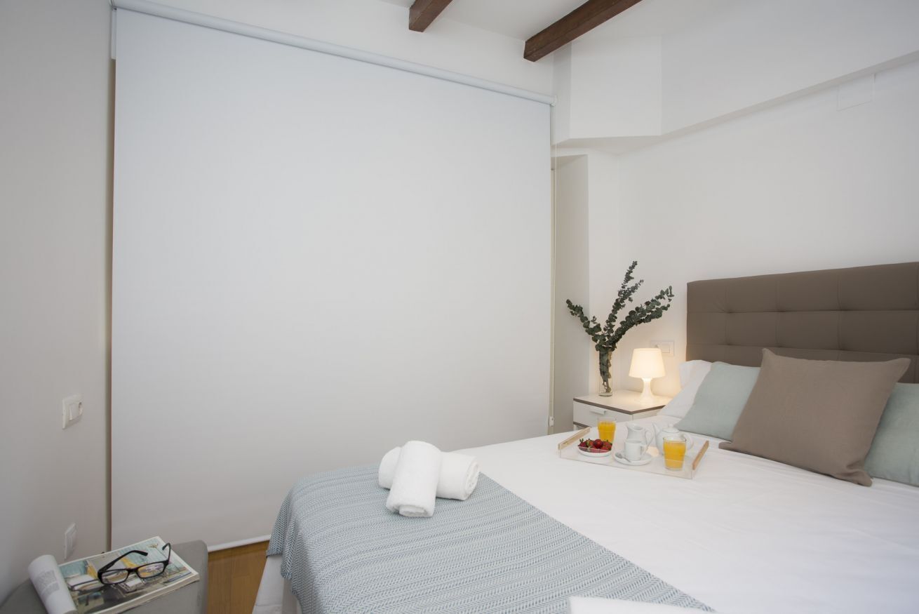 A hotel room with a bed, a bedside table with a tray of breakfast, a nightstand with a lamp, and a window with a view of the outside.