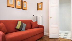 A red sofa with a striped pillow, a white radiator, and three framed pictures on the wall.