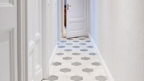 A hallway with white doors, a hexagonal patterned floor, and recessed ceiling lighting.