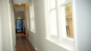 A hallway with white walls and wooden flooring, leading to a room with a window. - Ritz For Backpackers (St Kilda)