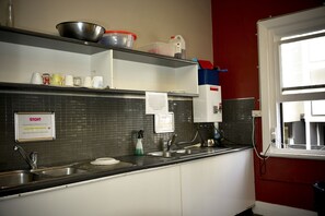 Une cuisine équipée d’un évier en acier inoxydable, d’un robinet, d’un distributeur de savon et d’une affiche accrochée au mur.