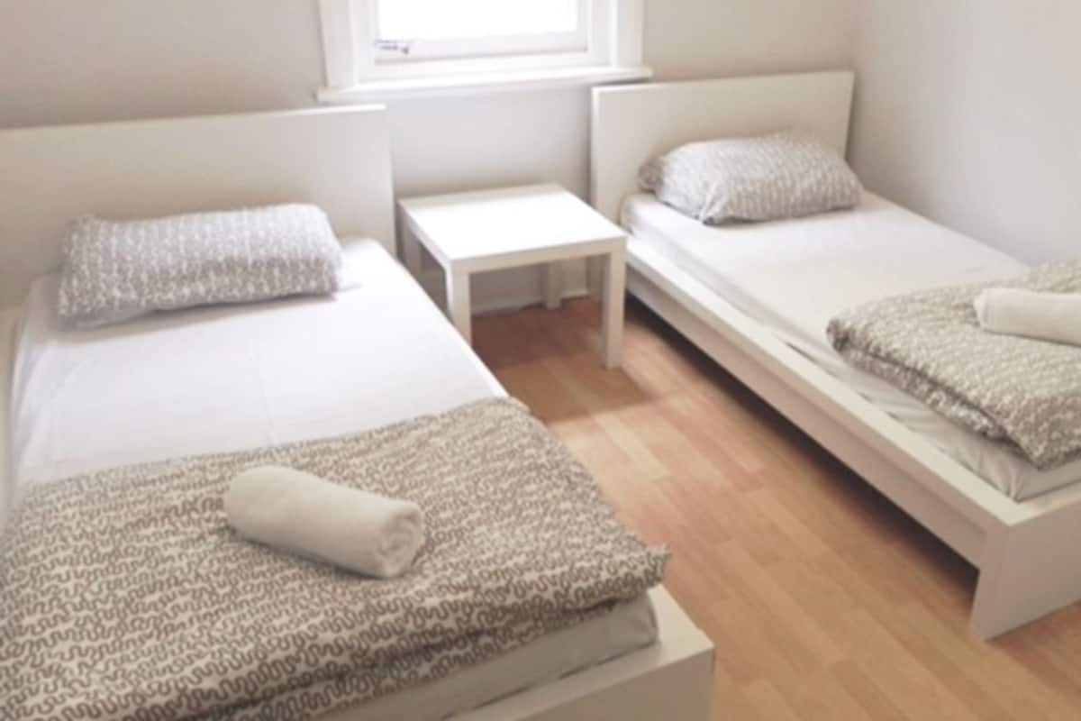 Ein Zimmer mit zwei Einzelbetten, einem kleinen Tisch und einem Fenster.