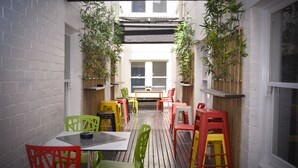 A narrow outdoor patio with a wooden deck, white brick walls, and a table with chairs. - Ritz For Backpackers (St Kilda)