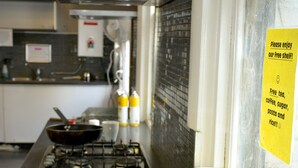 A kitchen counter with various food items and containers, a stove, and a sign offering free tea, coffee, sugar, pasta, and rice. - Ritz For Backpackers (St Kilda)