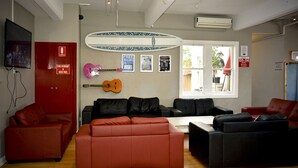 A living room with red and black sofas, a guitar, and a surfboard on the wall. - Ritz For Backpackers (St Kilda)