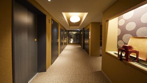 Un couloir d’hôtel avec un sol recouvert de moquette, des portes en bois foncé et un éclairage lumineux au plafond.
