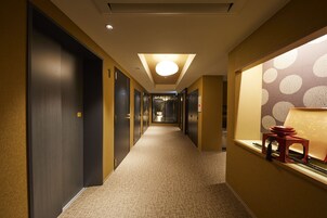 Un pasillo de hotel con piso alfombrado, puertas de madera oscura y una lámpara de techo brillante.