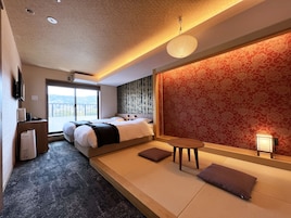 Una habitación de hotel con cama, una mesita y un sofá. Se aprecia una ventana con vistas al exterior.