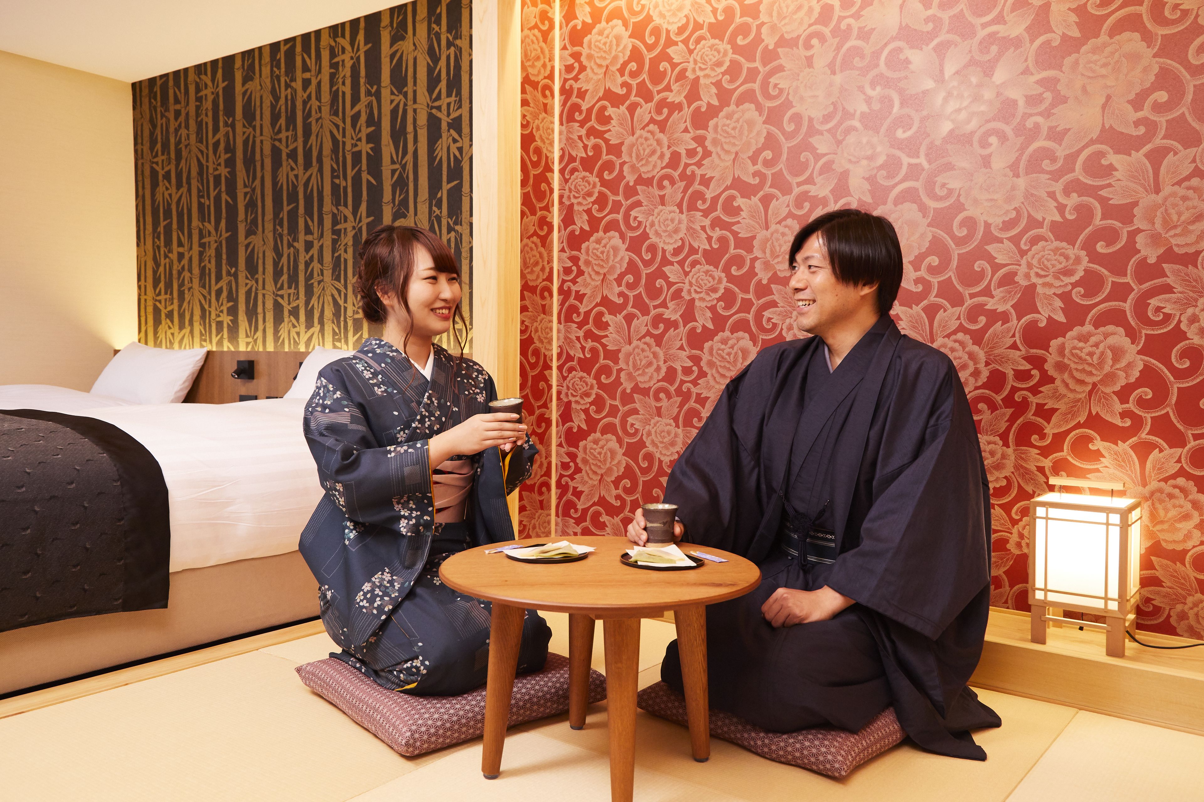 A traditional Japanese room with tatami flooring, a low table with two plates, and a bed with a dark headboard.