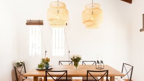 Uma área de refeições com uma mesa de madeira, seis cadeiras de fibra natural e duas luminárias de vime suspensas.