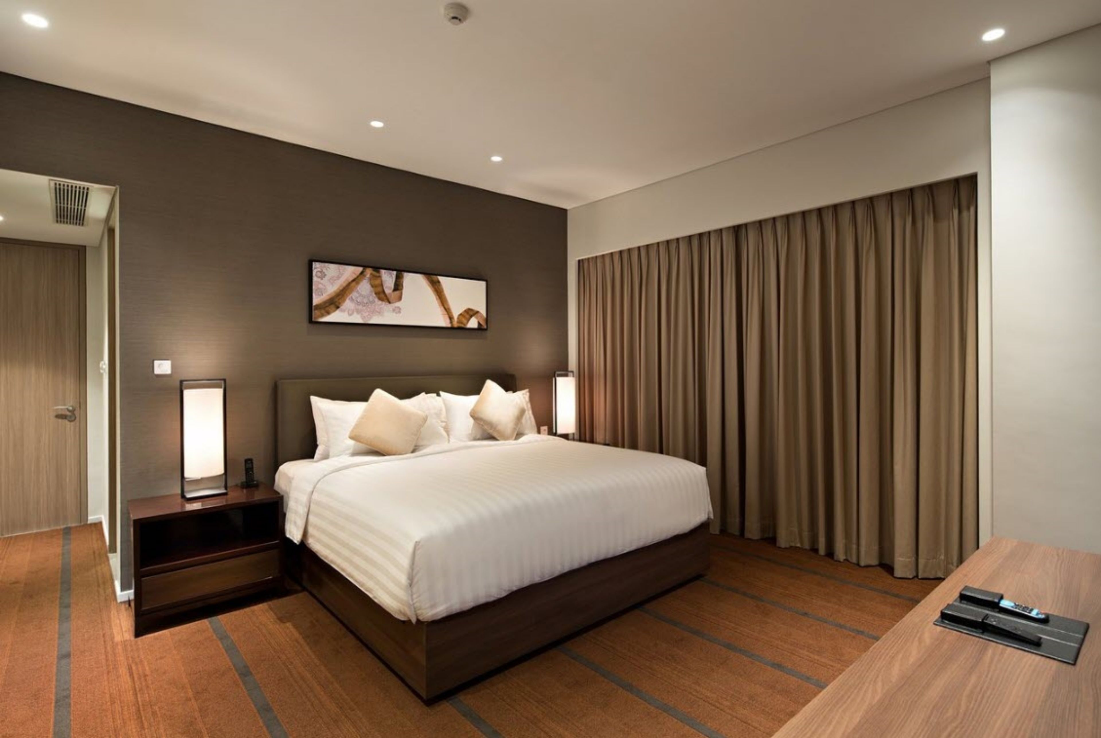 Une chambre d’hôtel moderne avec un grand lit, des lampes de chevet, un téléviseur à écran plat et une vue sur la ville, visible à travers les rideaux.