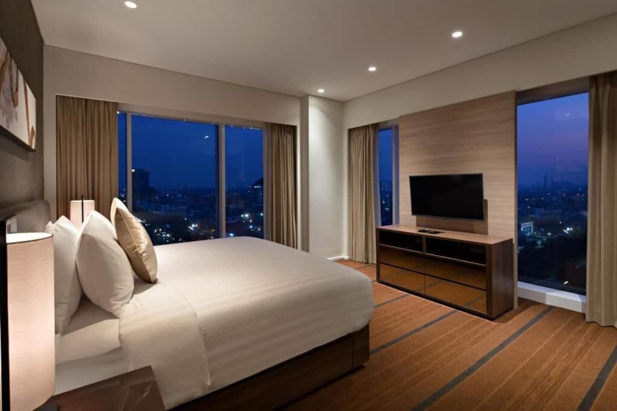 A hotel room with a large bed, a TV, and a view of the city at night.
