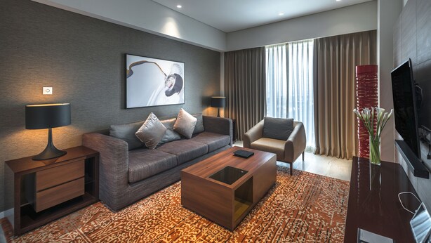 A modern living room with a sofa, armchair, coffee table, and a flat-screen TV. - Oakwood Hotel & Residence Surabaya (Surabaya)