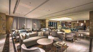 A spacious lobby with modern furniture, a central seating area, and a glass partition separating the lobby from the dining area.