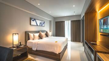 A modern hotel room with a large bed, a bedside table with a lamp, a TV mounted on the wall, and a large window with curtains.