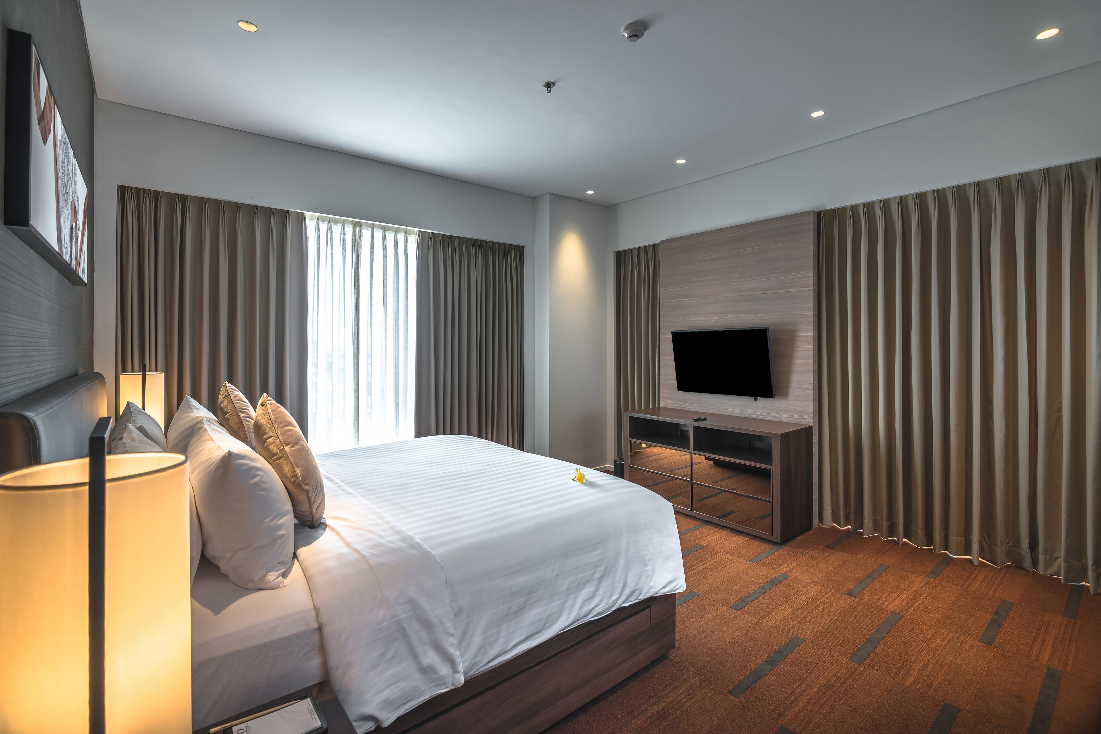 Una habitación de hotel moderna con una cama grande, un televisor de pantalla plana y piso de madera.