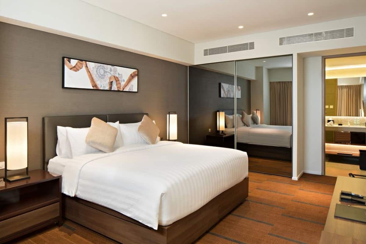 A modern hotel room with a large bed, bedside lamps, a mirror, and a painting on the wall.