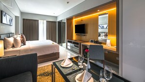 A modern hotel room with a large bed, a desk with a flat-screen TV, and a seating area with a table set for two.