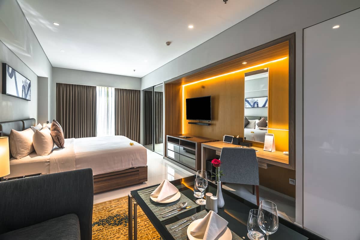 A modern hotel room with a large bed, a desk with a flat-screen TV, and a seating area with a table set for two.