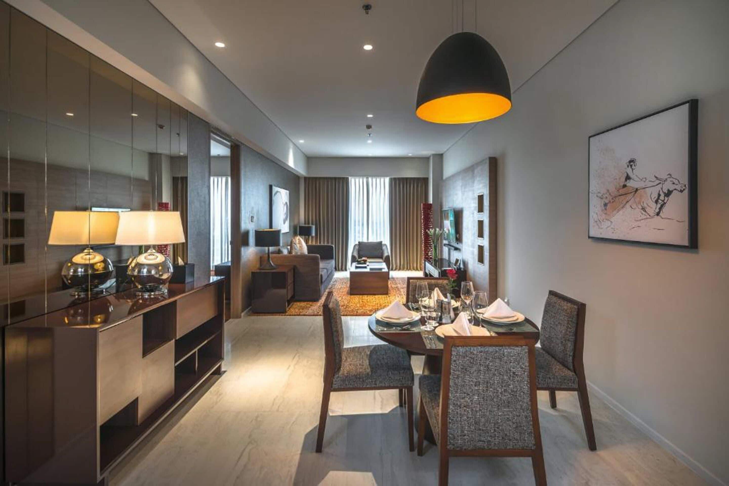 A modern hotel room with a dining area, a living room, and a large mirror.