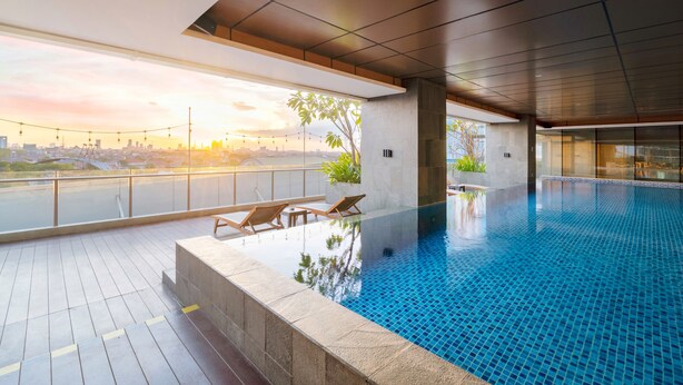 An indoor swimming pool with a city view, lounge chairs, and a tiled deck.