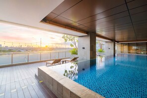 An indoor swimming pool with a city view, lounge chairs, and a tiled deck. - Oakwood Hotel & Residence Surabaya (Surabaya)