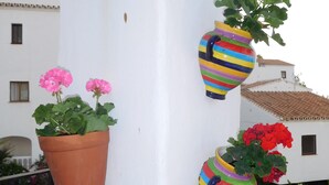 Eine weiße Säule mit drei bunten hängenden Pflanzgefäßen, in denen verschiedene Blumen blühen.