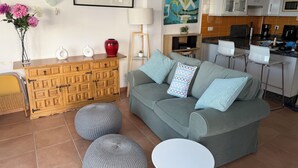 Ein Wohnzimmer mit grauem Sofa, runden Hocker, einem Holzschrank und einem Gemälde an der Wand.