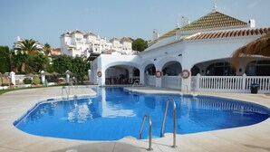 Ein Schwimmbecken mit klarem, blauem Wasser, umgeben von einer gefliesten Terrasse und weißen Gebäuden mit Rundbogenfenstern im Hintergrund.