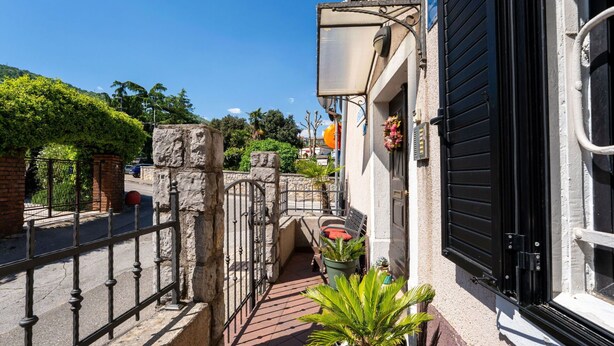 A narrow alleyway with a stone gate, potted plants, and a building with a black shutter door.