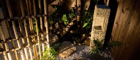 Un giardino con recinto in bambù, rocce e un palo di legno.
