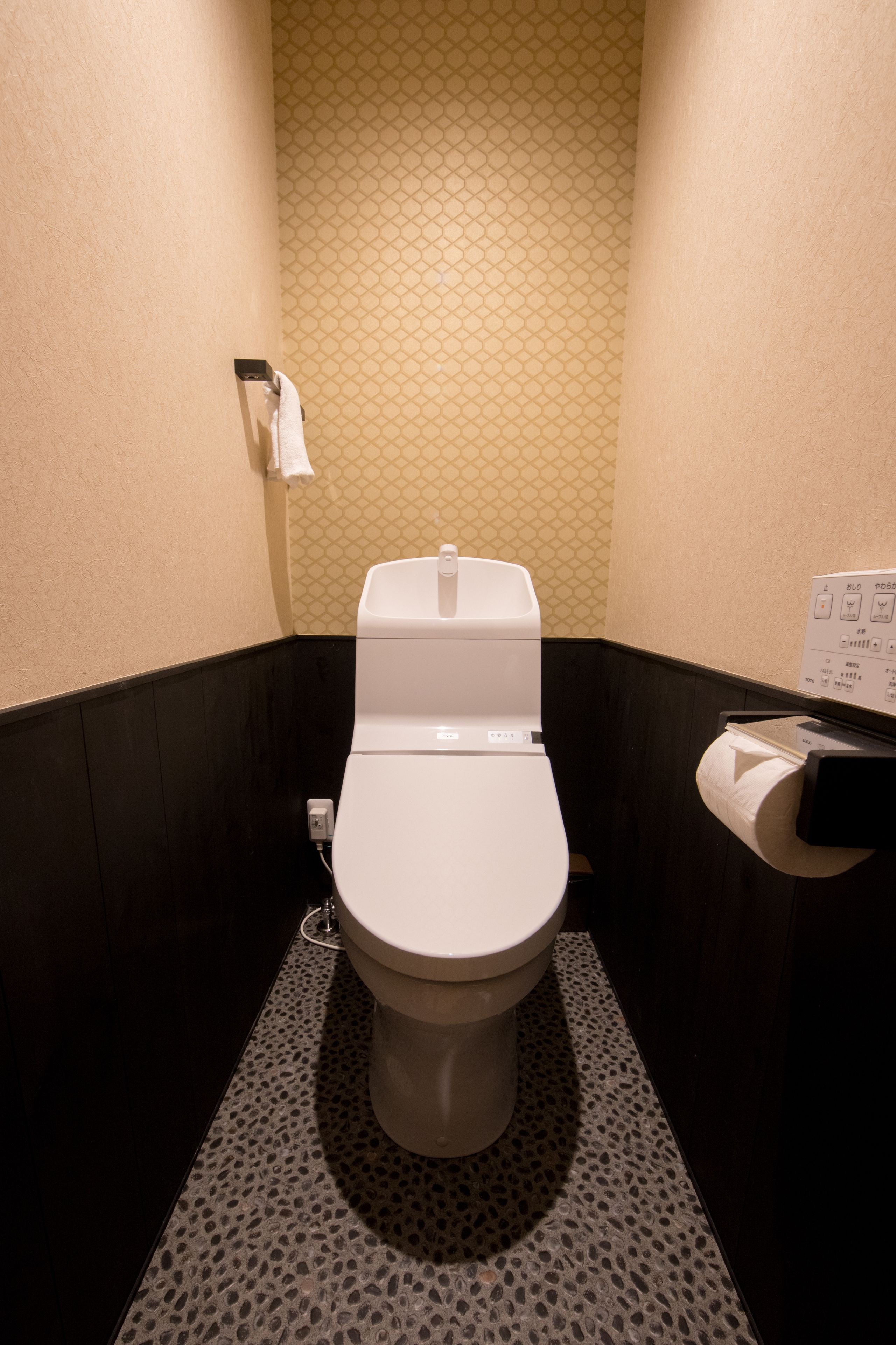 A modern bathroom with a toilet, a paper towel dispenser, and a patterned wall.