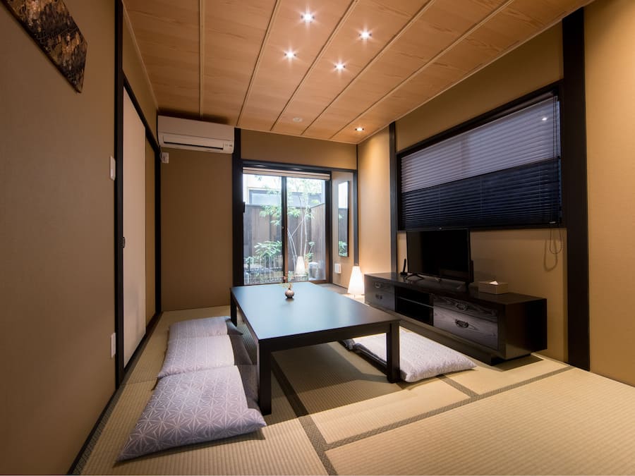Um quarto em estilo japonês tradicional, com piso de tatame, uma mesa baixa, um armário e uma porta deslizante que dá para uma varanda.