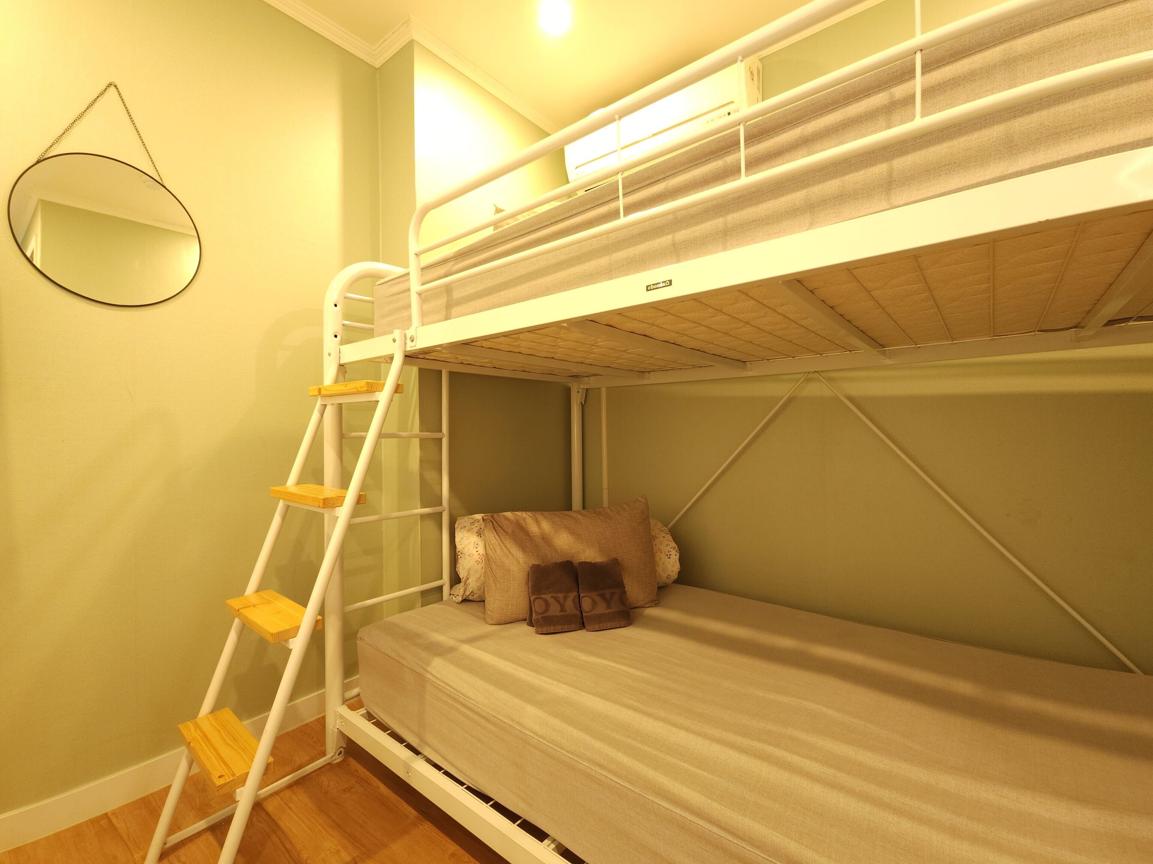 A bunk bed room with a ladder, a pillow, and a wall-mounted mirror.