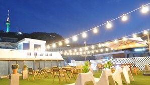 An outdoor seating area with tables and chairs, string lights, and potted plants. - OYO Rooftop Hostel (Seoul)