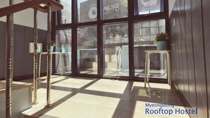 A hostel interior with large windows, metal railings, and a tiled floor. - OYO Rooftop Hostel (Seoul)