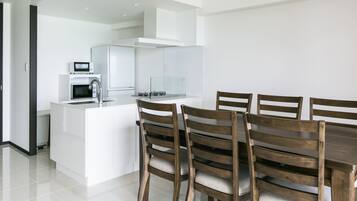 Una cocina moderna con armarios blancos, horno integrado y microondas. Hay una mesa de comedor con sillas de madera.