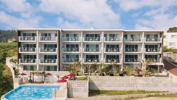 A multi-story hotel with a pool area, outdoor seating, and a view of the surrounding landscape.