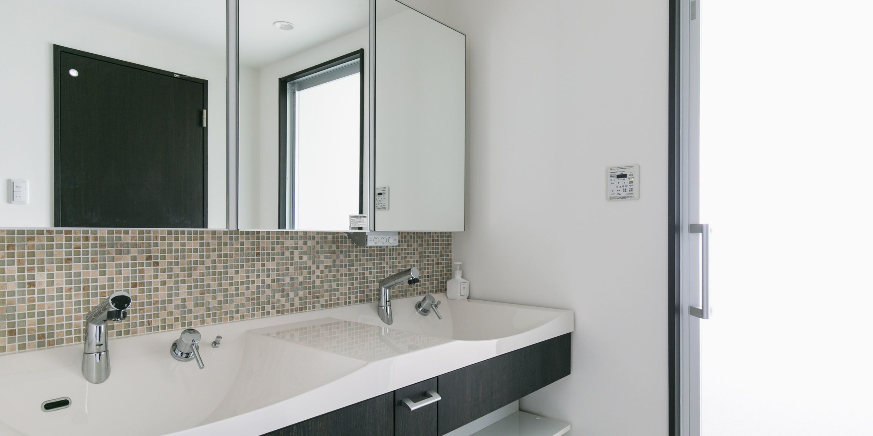 A modern bathroom with a large mirror, two sinks, and a tiled backsplash.