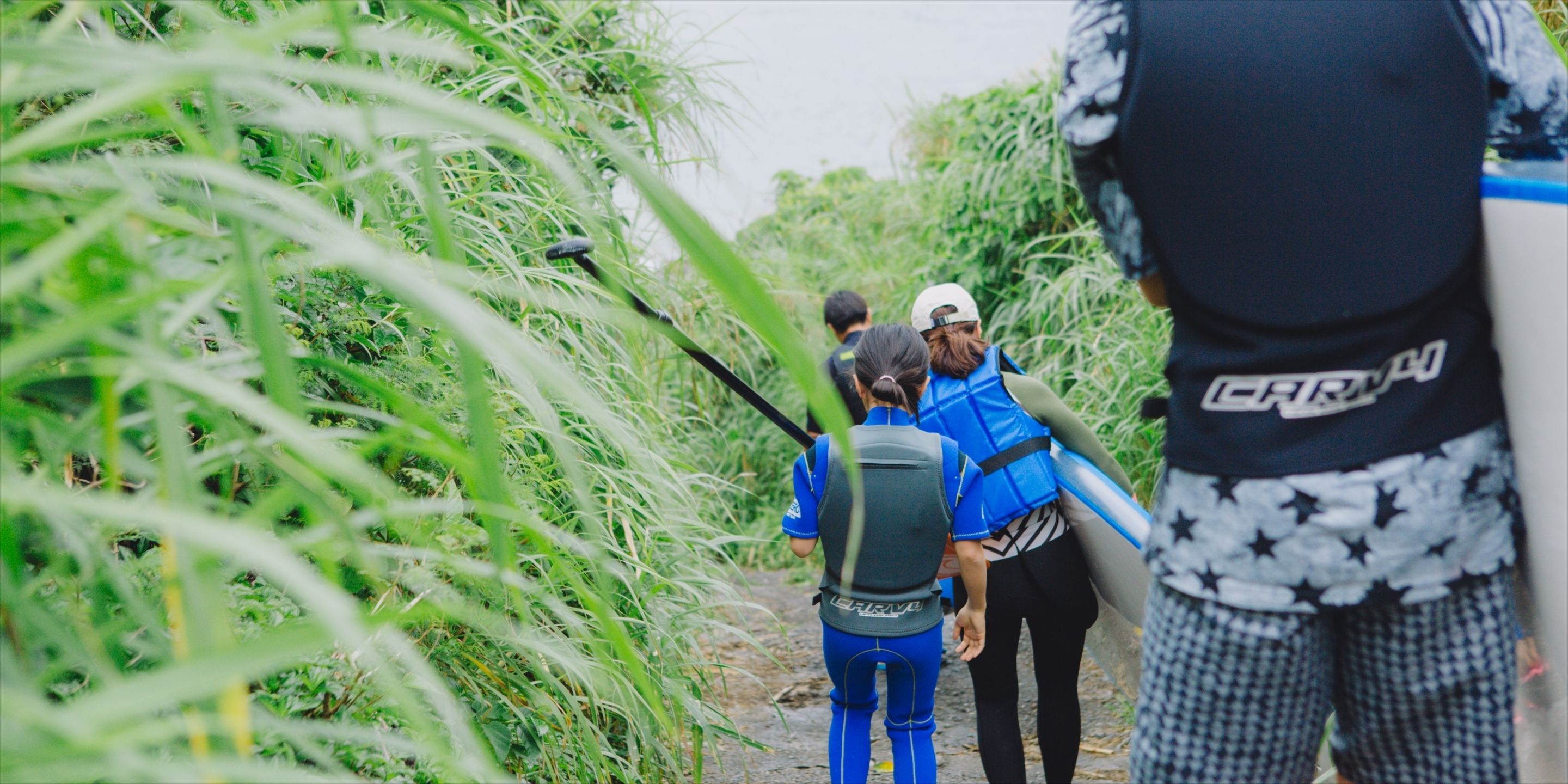 A group of people walking through a narrow path surrounded by tall grass and vegetation.