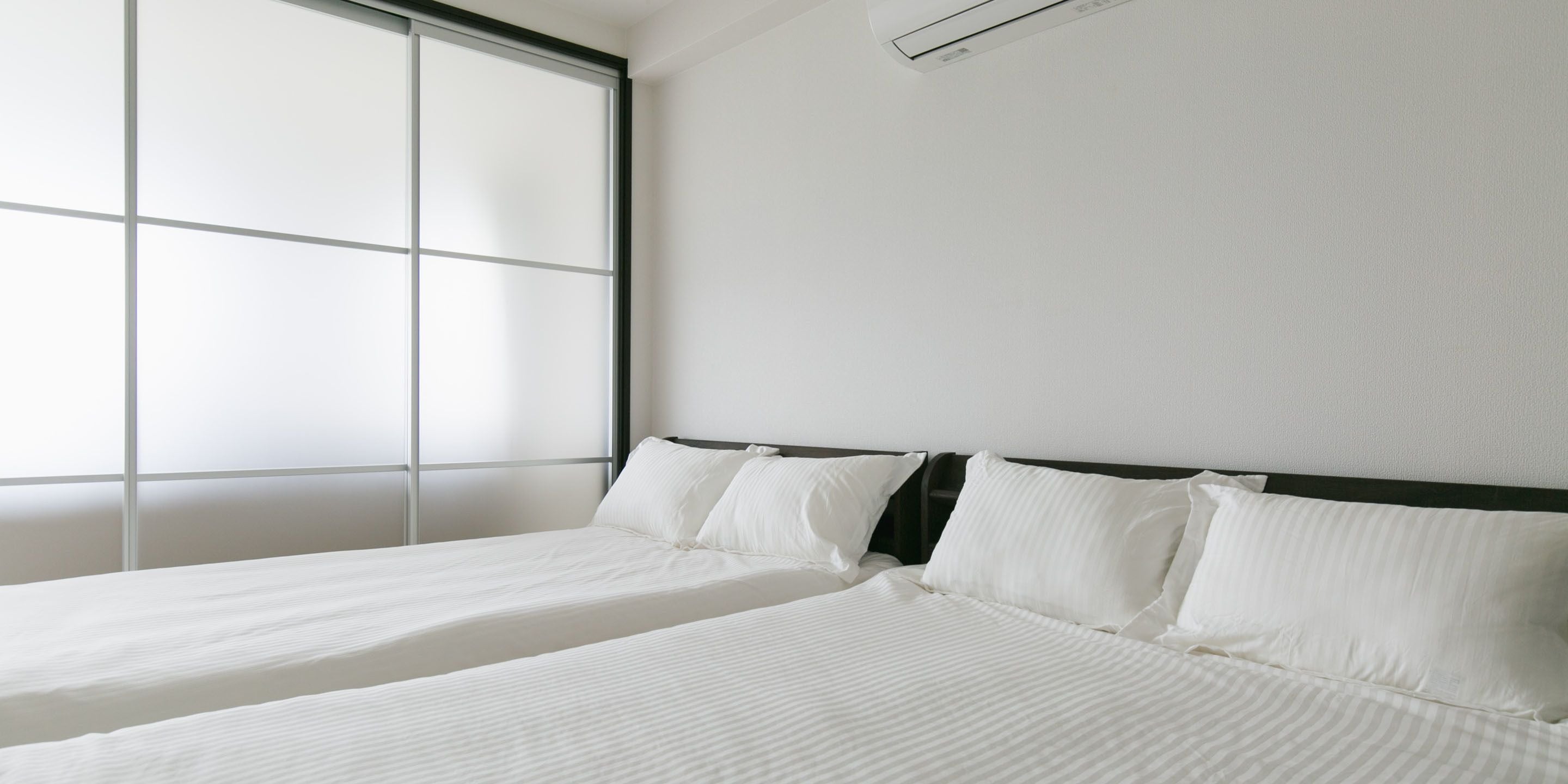 Une chambre d’hôtel avec deux lits, une grande fenêtre et un climatiseur fixé au mur.