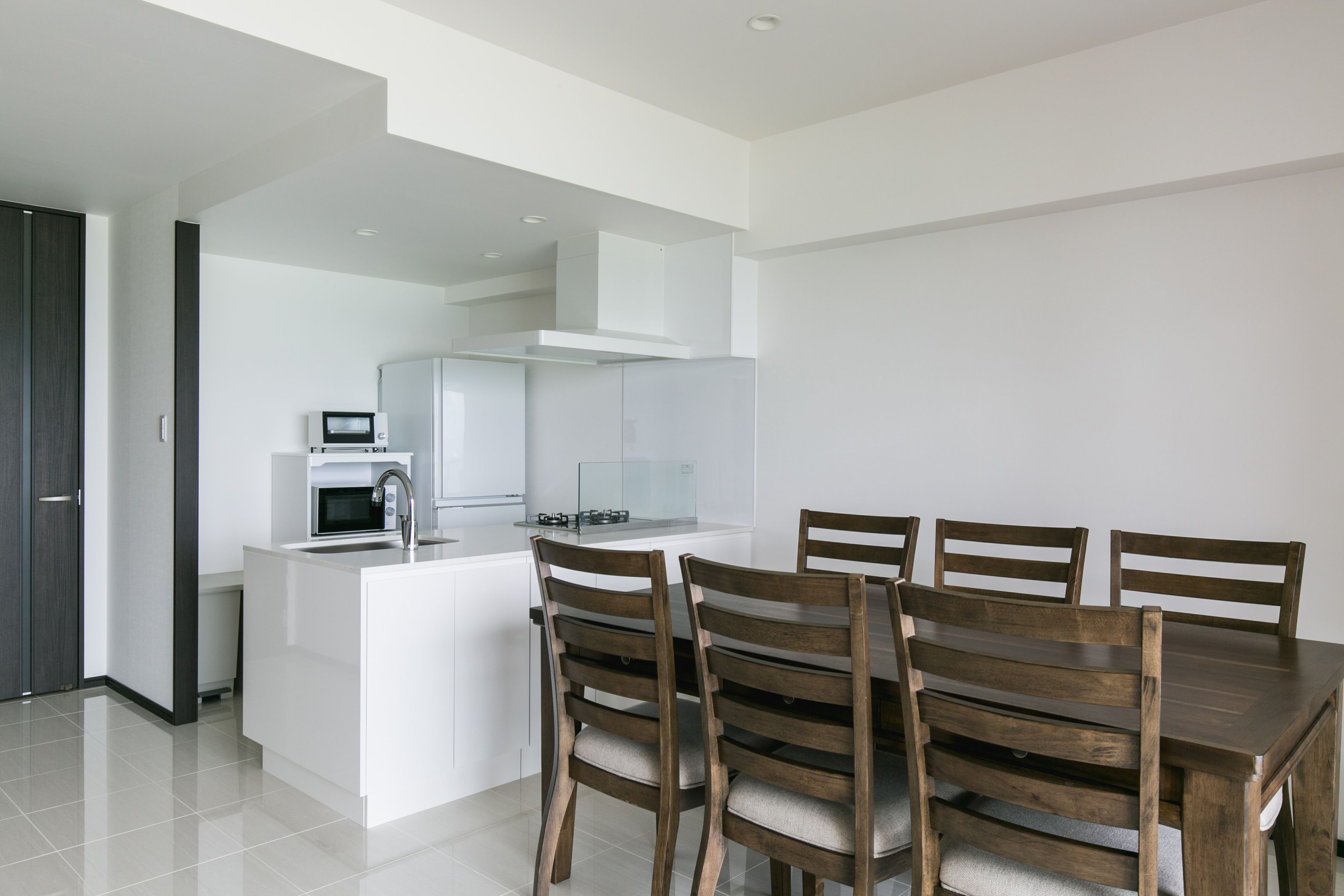 A modern kitchen with white cabinetry, a central island with a sink, and a dining area with wooden chairs.