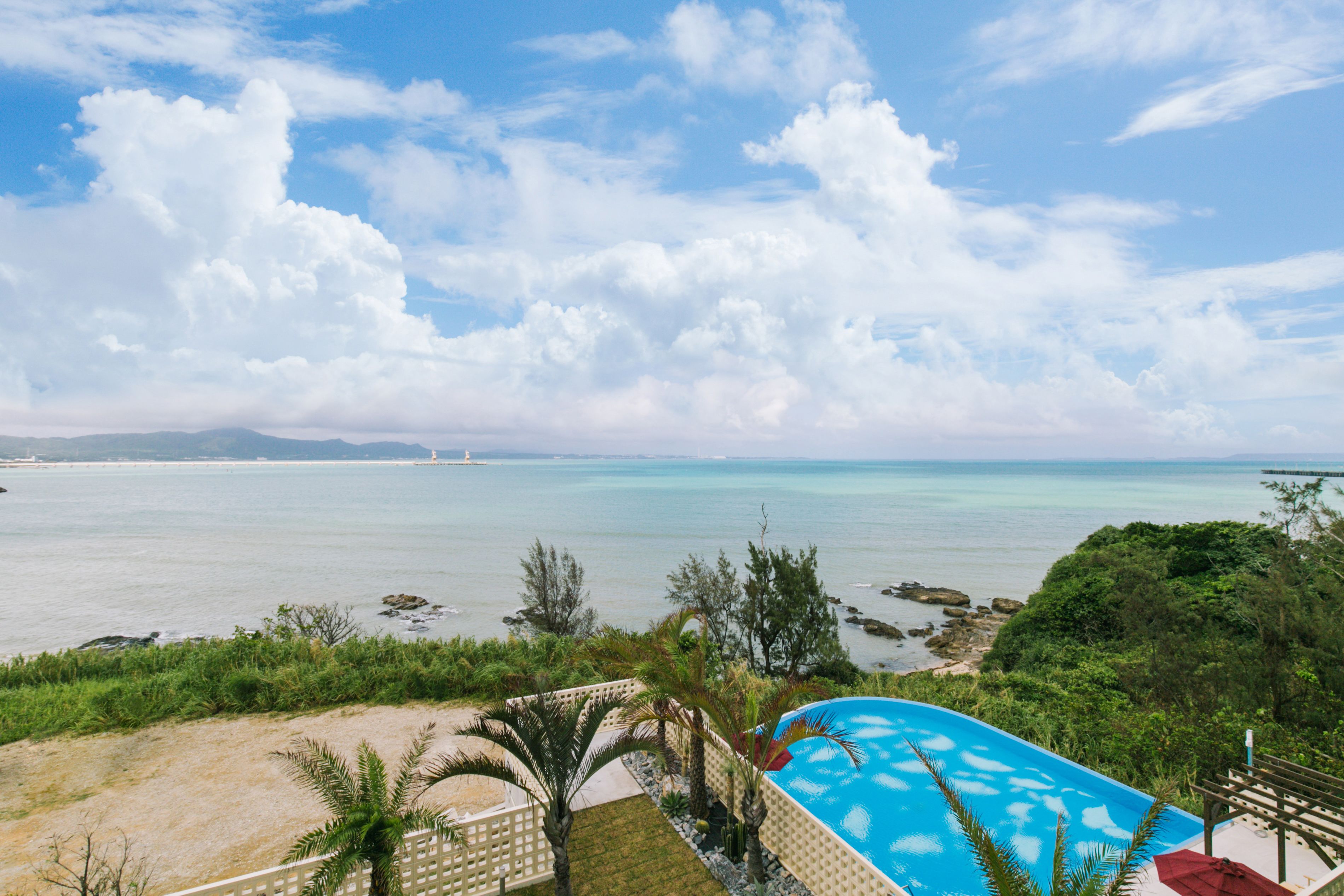 A pool with a view of the sea, surrounded by greenery and a clear sky.
