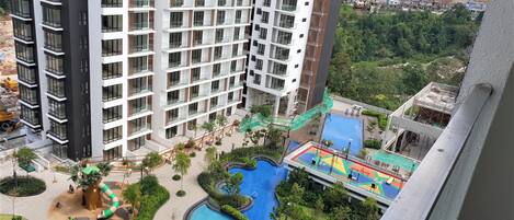 A high-rise hotel with multiple balconies, a swimming pool, and a children's play area.