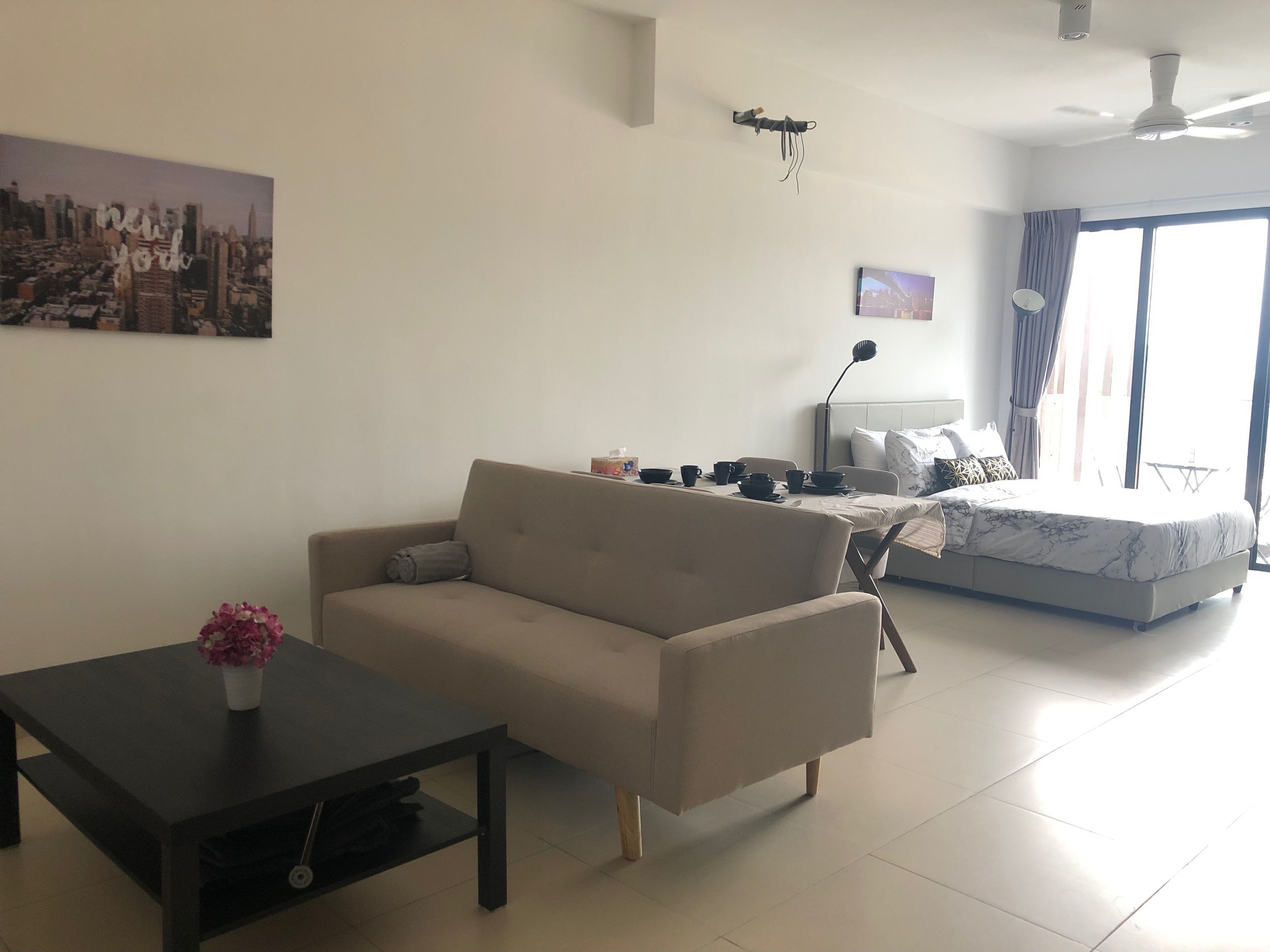 Ein modernes Wohnzimmer mit Sofa, Couchtisch und Esstisch, gedeckt mit Tassen und Schüsseln. Ein Bett mit weißer Bettdecke und ein Stadtbild an der Wand sind ebenfalls zu sehen.