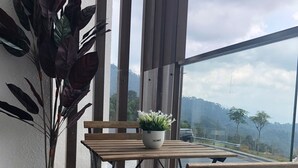 Un balcon avec une table et des chaises en bois, un pot de fleurs et une vue sur une route et des montagnes.