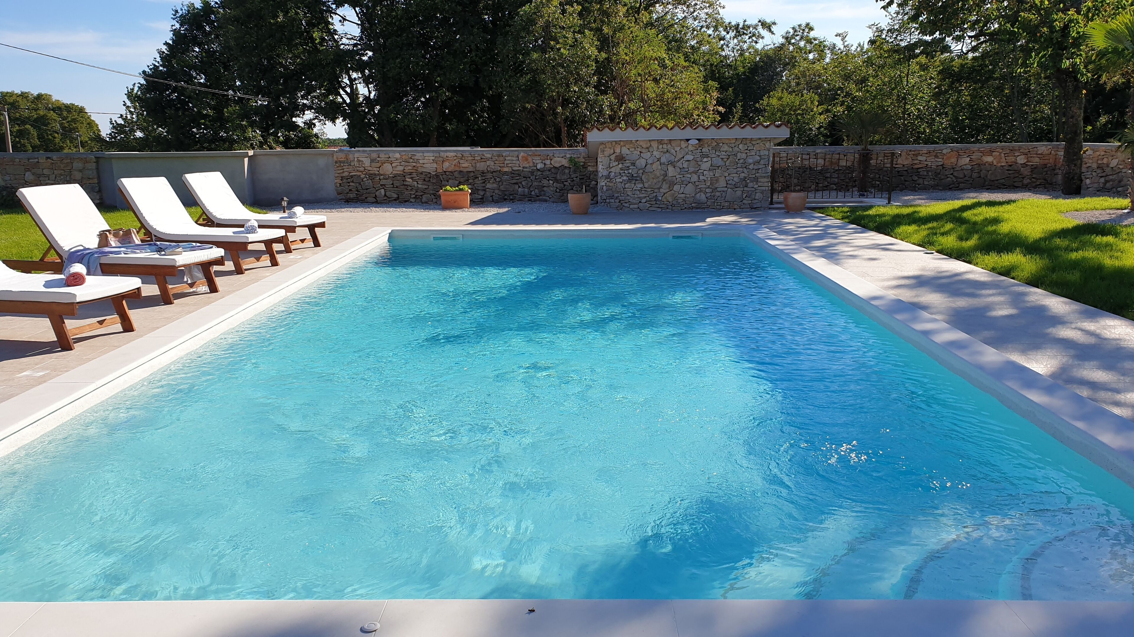 Ein rechteckiger Swimmingpool mit klarem, blauem Wasser, umgeben von Liegestühlen und einer Steinmauer.