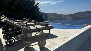 A rooftop terrace with lounge chairs and a pool overlooking a scenic view of the sea and mountains.