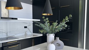 A modern kitchen with black cabinets, a white marble countertop, two pendant lights, and a vase with greenery.