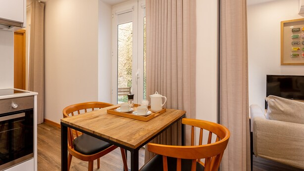 Un comedor con una mesa de madera, dos sillas, una bandeja con una jarrilla y tazas, y vistas a través de una ventana.